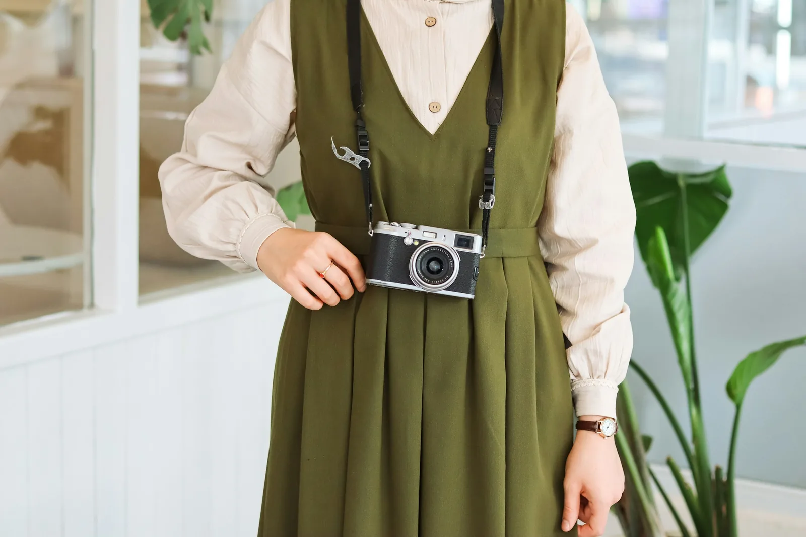 Fashion model in an olive green pinafore dress holding a vintage film camera on a strap